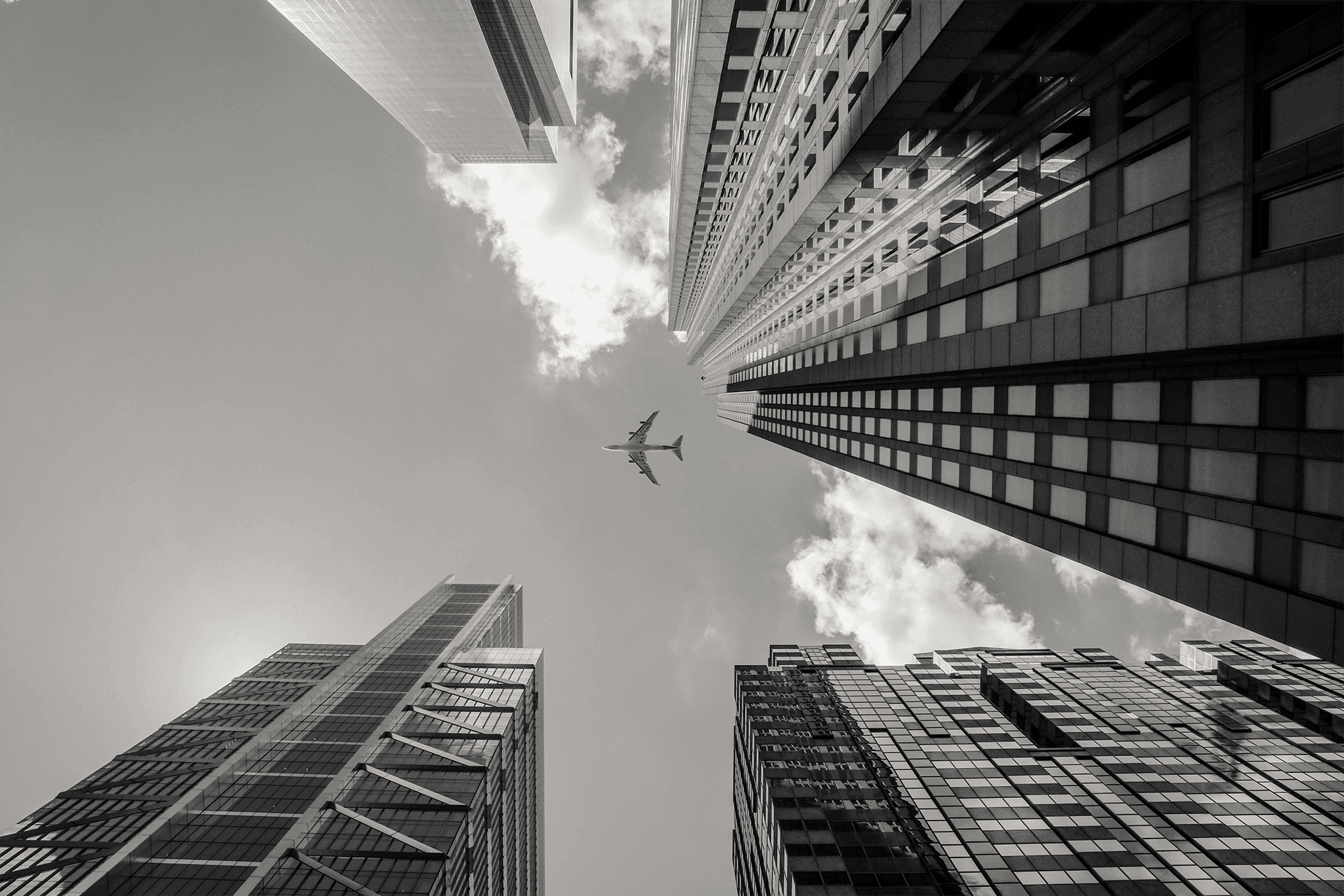 low-angle-greyscale-shot-airplane-flying-high-rise-buildings